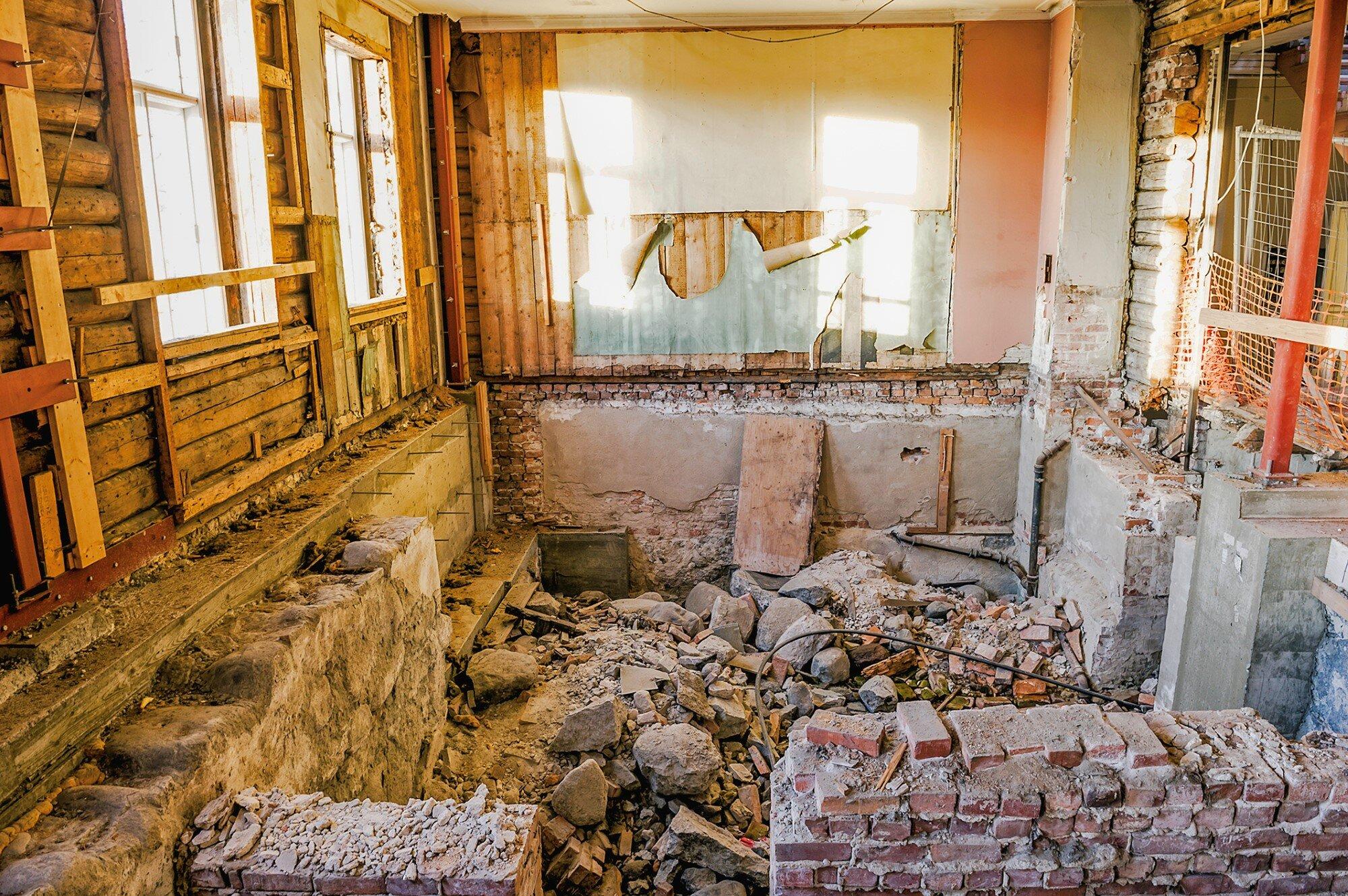 Forfallent rom uten gulv og med hauger av murstein, stein, grus og byggematerialer.