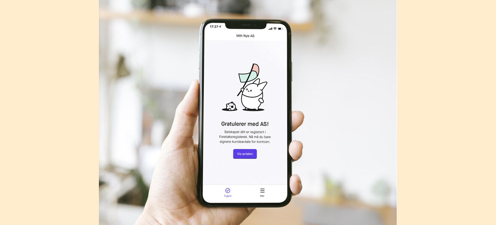 Et foto av en hånd som holder opp en mobiltelefon vendt med skjermen mot kamera. På skjermen ses en søt liten kaninmaskot og meldingen "gratulerer med AS!".