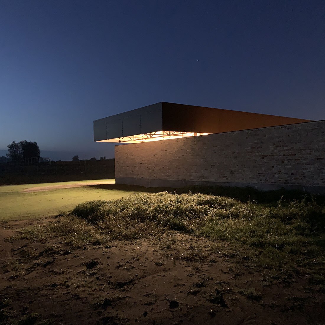 Bilde tatt på nattestid: en metallkonstruksjon stikker ut over en murvegg. I overhenget er det montert lys, som lyser opp veggen og vegetasjonen rundt.