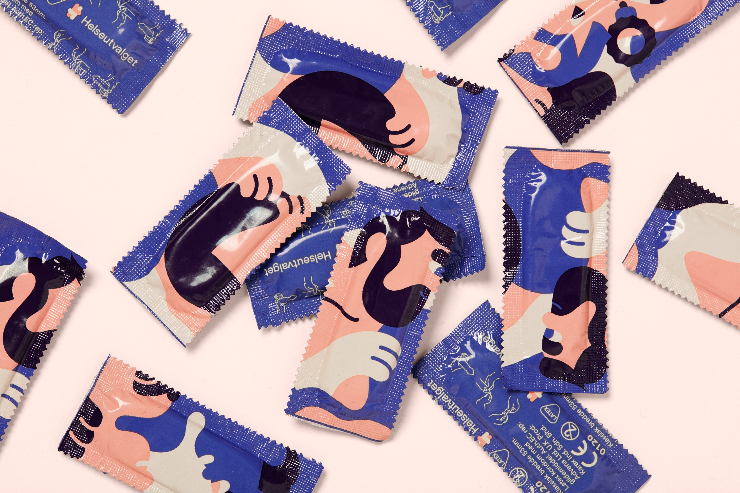 Kondomer i innpakning spredt utover et bord. Emballasjen har utsnitt av en semiabstrakt illustrasjon.