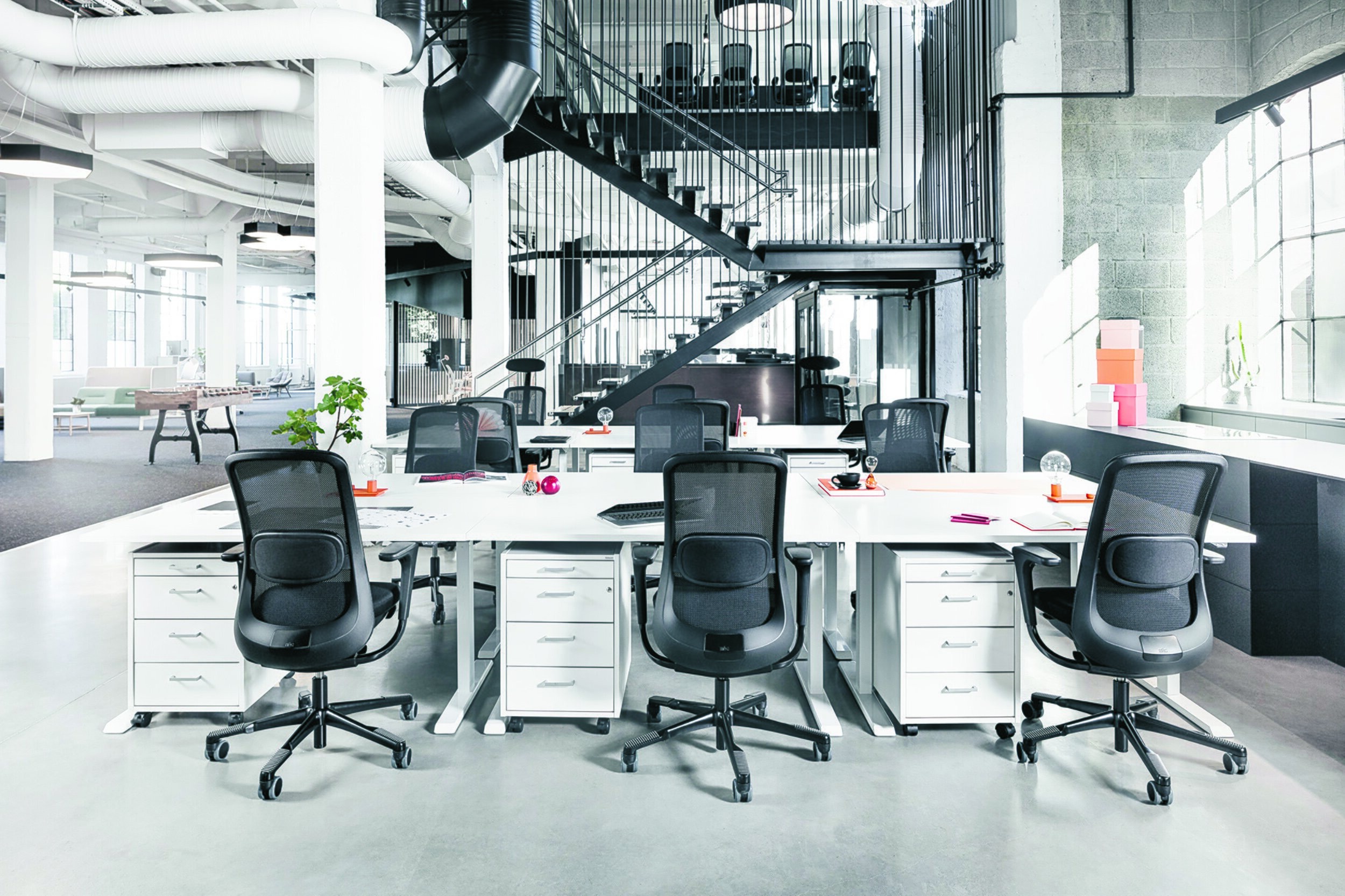 Bildet viser et kontorlandskap hvor det mest fremtredende er ryggene til tre svarte kontorstoler langs en lang hvit arbeidspult.
