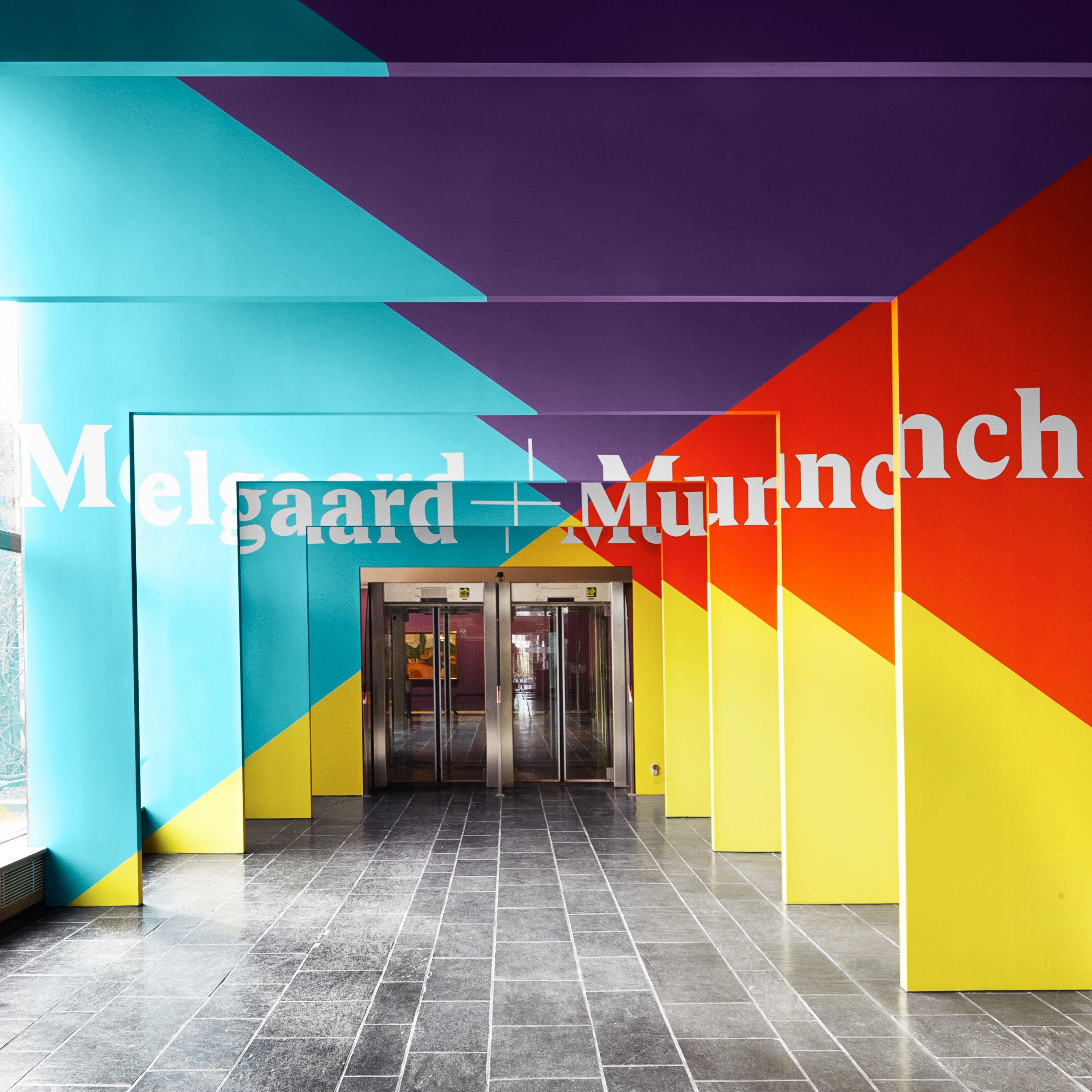 En lang gang er innrammet av fargerike portaler som sammen staver "Melgaard+Munch". Det fremstår som en inngang til utstillingen.