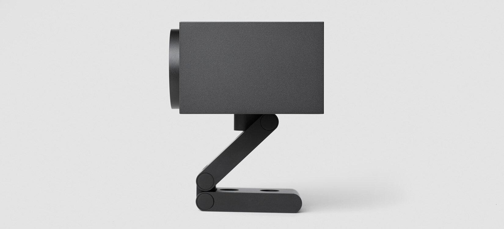 Produktrender av et kamera fra siden. Kamera står på en fot i Z-form. Skarpe kanter og rette linjer.