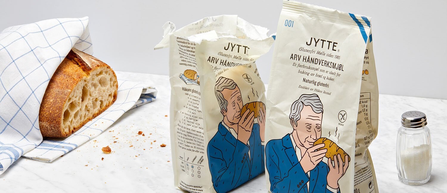 Bildet viser to pakker mel, en åpen, i et stilleben med et brød i en kjøkkenhånkle og en saltbøsse. Emballasjen har en illustrasjon av en mann i blå dressjakke som lukter på et nybakt brød.