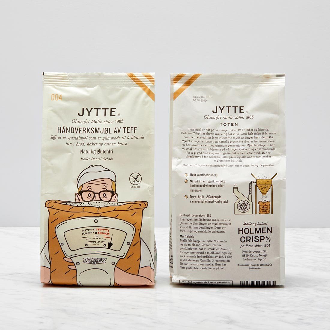 Bildet viser to pakker Jytte mel, en med forsiden mot kamera, og en med baksiden mot kamera. Illustrasjonen på emballasjen er av en mann med bakerhatt som så vidt er synlig bak en stor sekk med korn som han holder på.