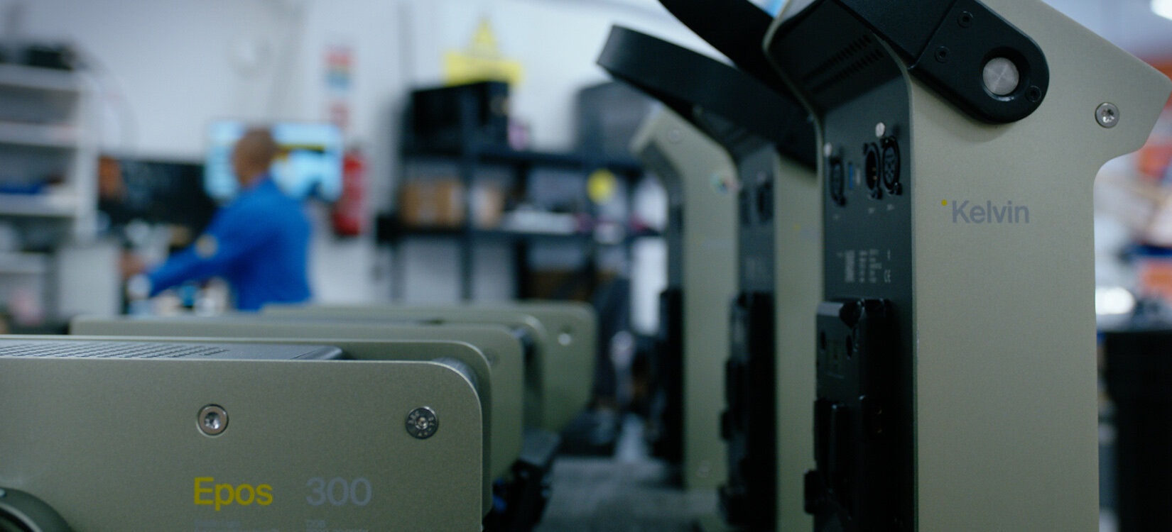 Rekke med Kelvin Epos 300-filmlamper på et arbeidsbord, med verkstedmiljø i bakgrunnen.