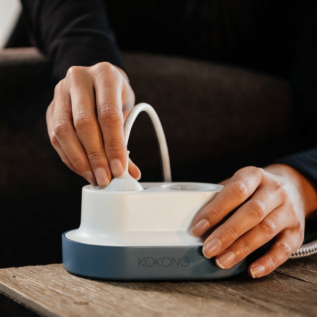 Nærbilde av to hender som setter et støpsel i en hvit forgrener med koksgrå base påskrevet "KOKONG".