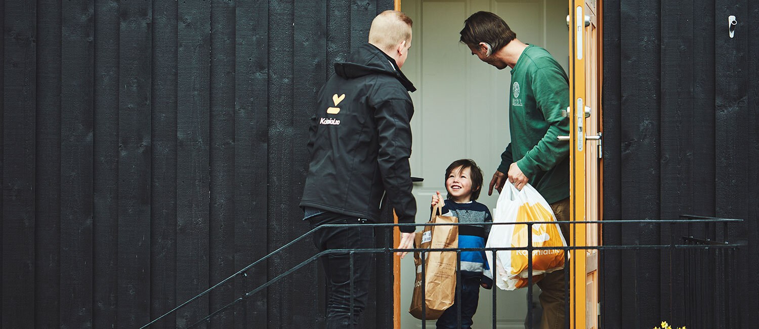 Et bud i sort uniform leverer matvarer på døren til en mann og et barn.