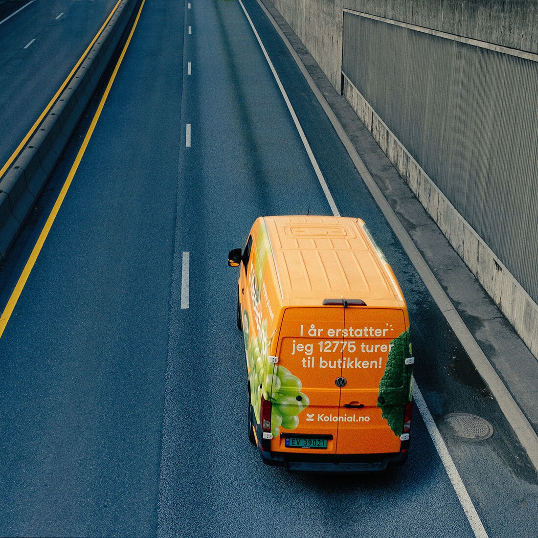 Bildet viser en gulfoliert varebil på en vei. Bilen har påskrevet: "I år erstatter jeg 12775 turer til butikken!" og "kolonial.no".