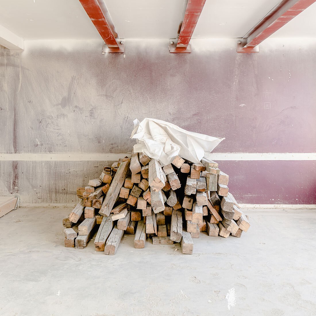 En stabel originale trebjelker er plassert i et rom som ser ut til å være i oppussing.