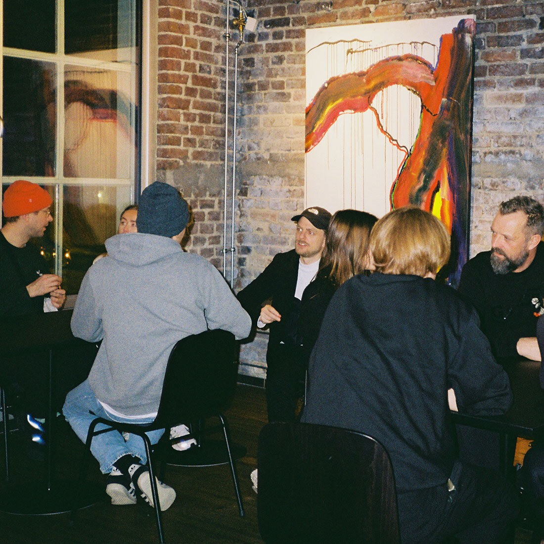 En gruppe mennesker i sosial setting, sittende rundt to bord, i samtaler.