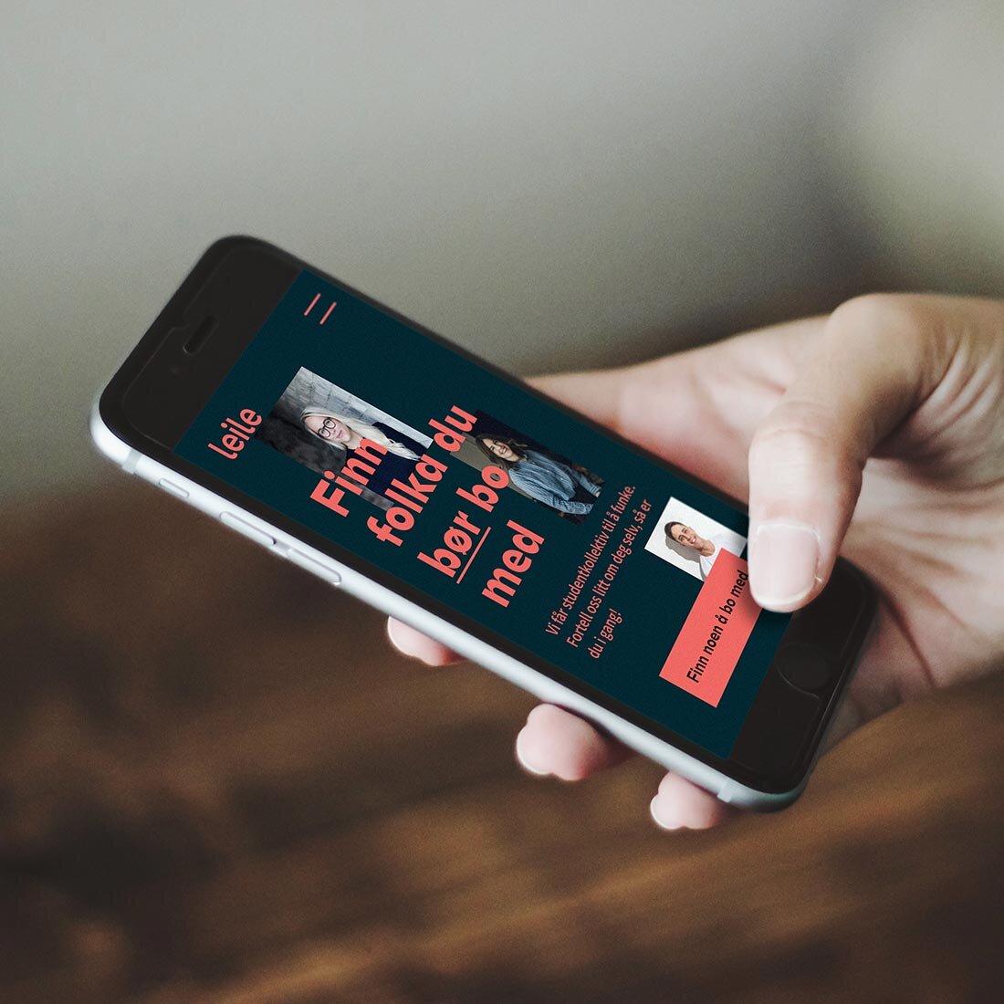 En hånd som holder en smarttelefon med Leiles nettside.