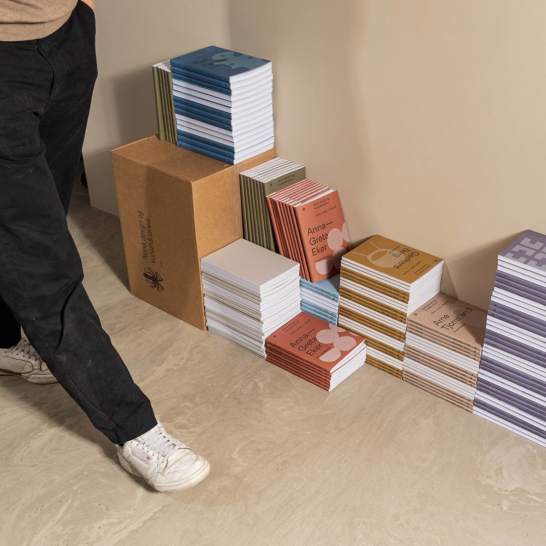 Stabler av bøker og bokomslag på gulvet ved siden av pappesker.