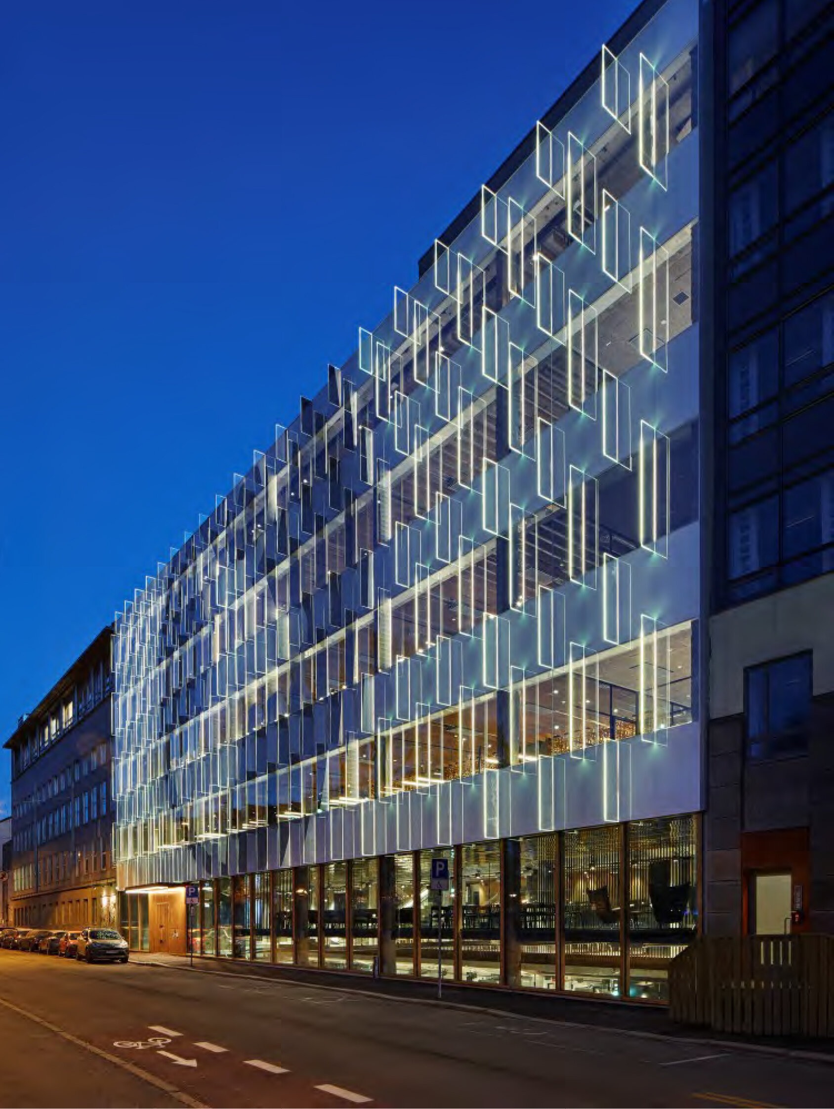 Bilde tatt av en bygningsfasade fra gateplan. Glasspaneler stikker ut fra fasaden, reflekterer lys og skaper et spill i uttrykket.