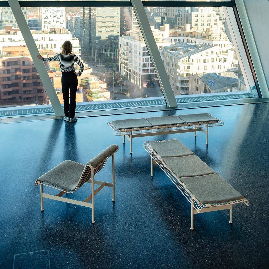 En lounge-stol og to benker fotografert fra inni munchmuseet. I bakkanten av bildet er det store vinduer og en kvinne som ser utover den tette bebyggelsen i Barcode i Oslo.