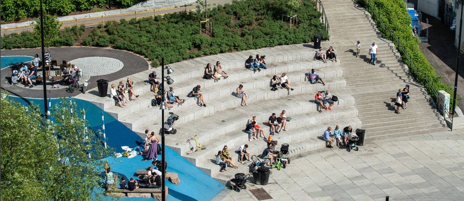 Vi ser et byrom fra fugleperspektiv. Sentralt i bildet er et sitteamfi i stein med beplantning i bakkant. Til høyre er et trappeløp. Til venstre i bildet ses gummiert fallunderlag i ulike nyanser av blå.