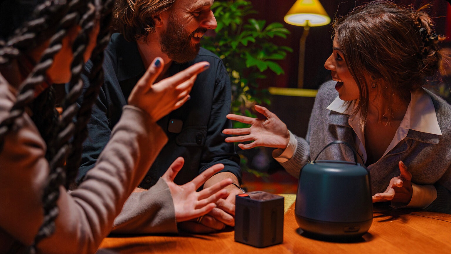 Tre voksne sitter rundt et bord i engasjert samtale med lydopptakeren Nomono på bordet.