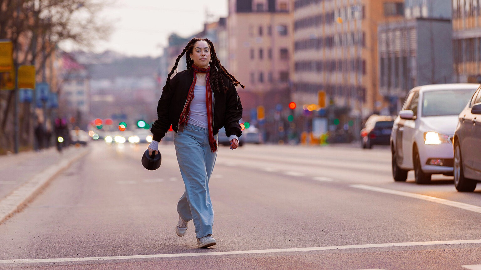 Jente med lange fletter går ute i gata med en Nomono-boks i hånda.