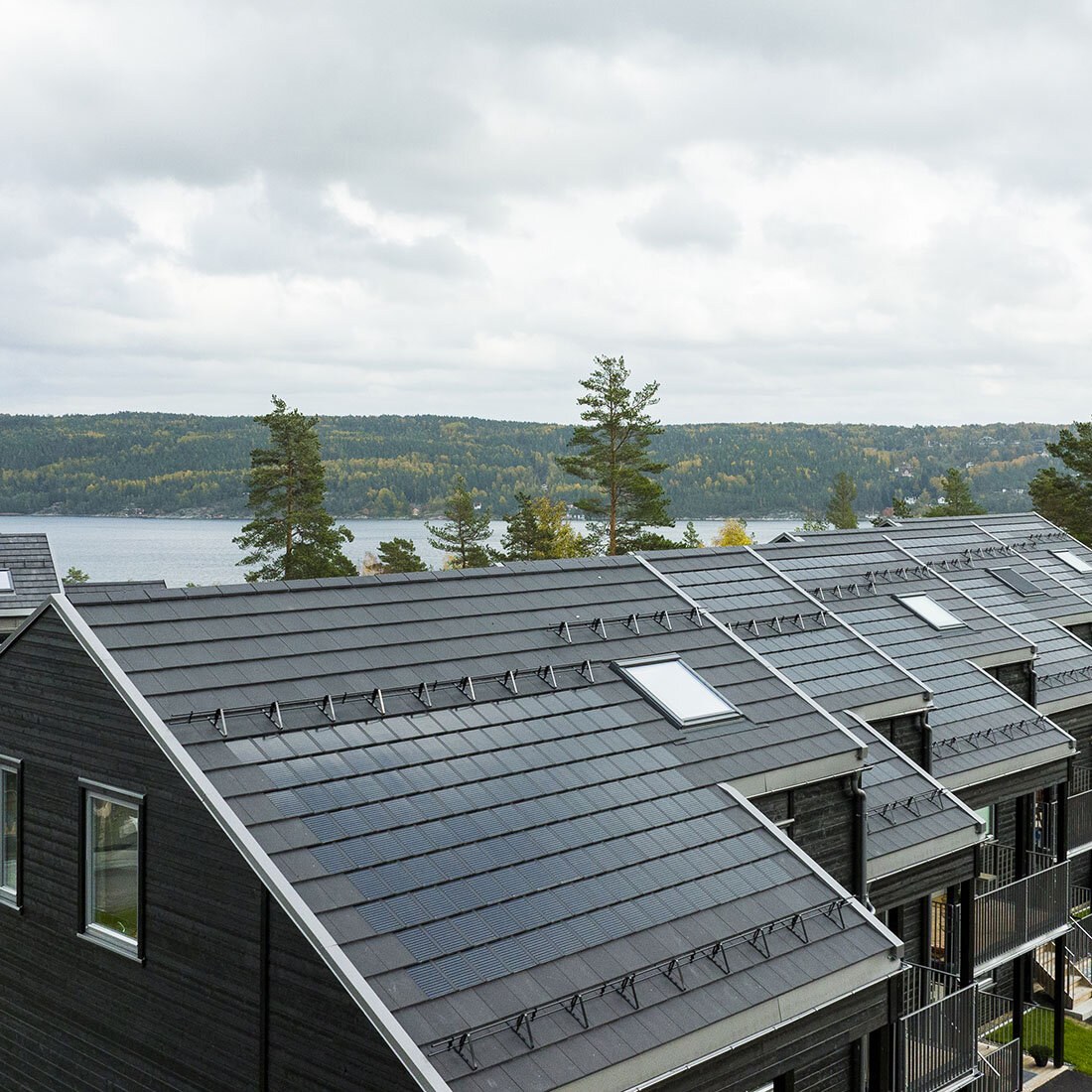 En rekke med hustak sett fra moderat fugleperspektiv. Husene har grå moderne tak, og enkelte steder er taksteinene blankere, noe som indikerer at de har solceller.