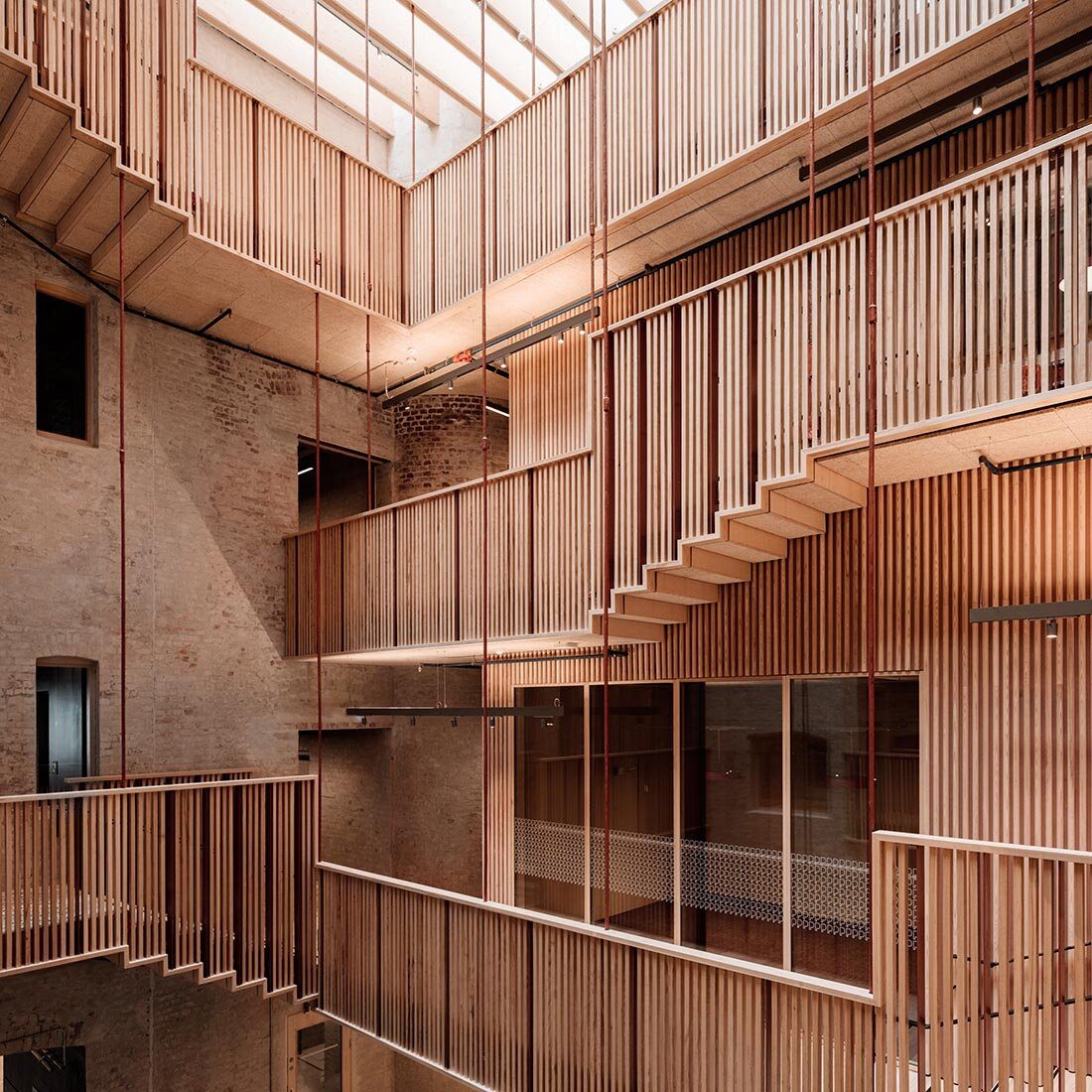 Vi ser et atrie med flere trappeløp og gangbroer med lyse spilegjerder langs teglesteinsvegger. Naturlig lys slipper ned fra taket.