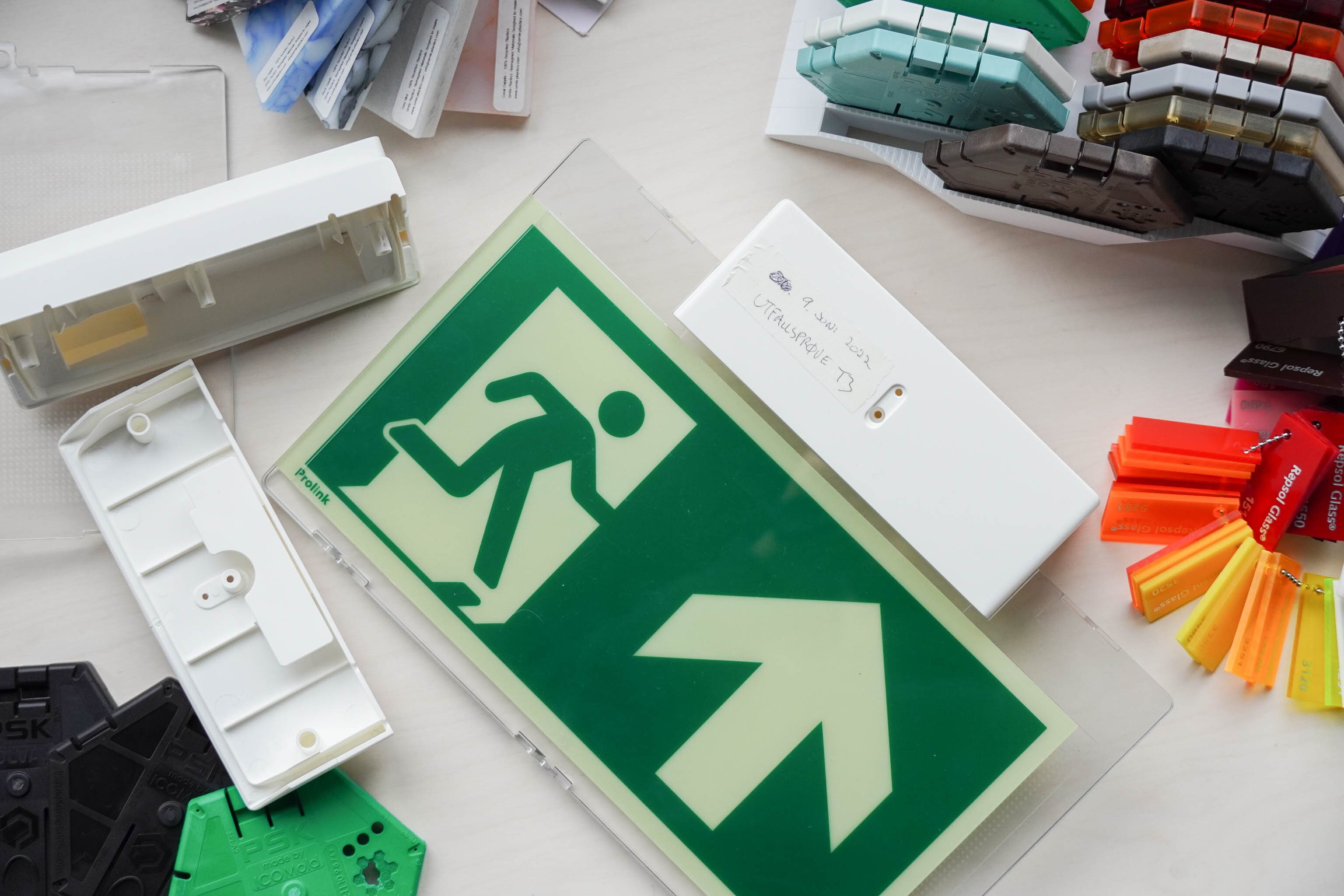 Nødutgangsskilt ligger på et bord med materialprøver rundt.