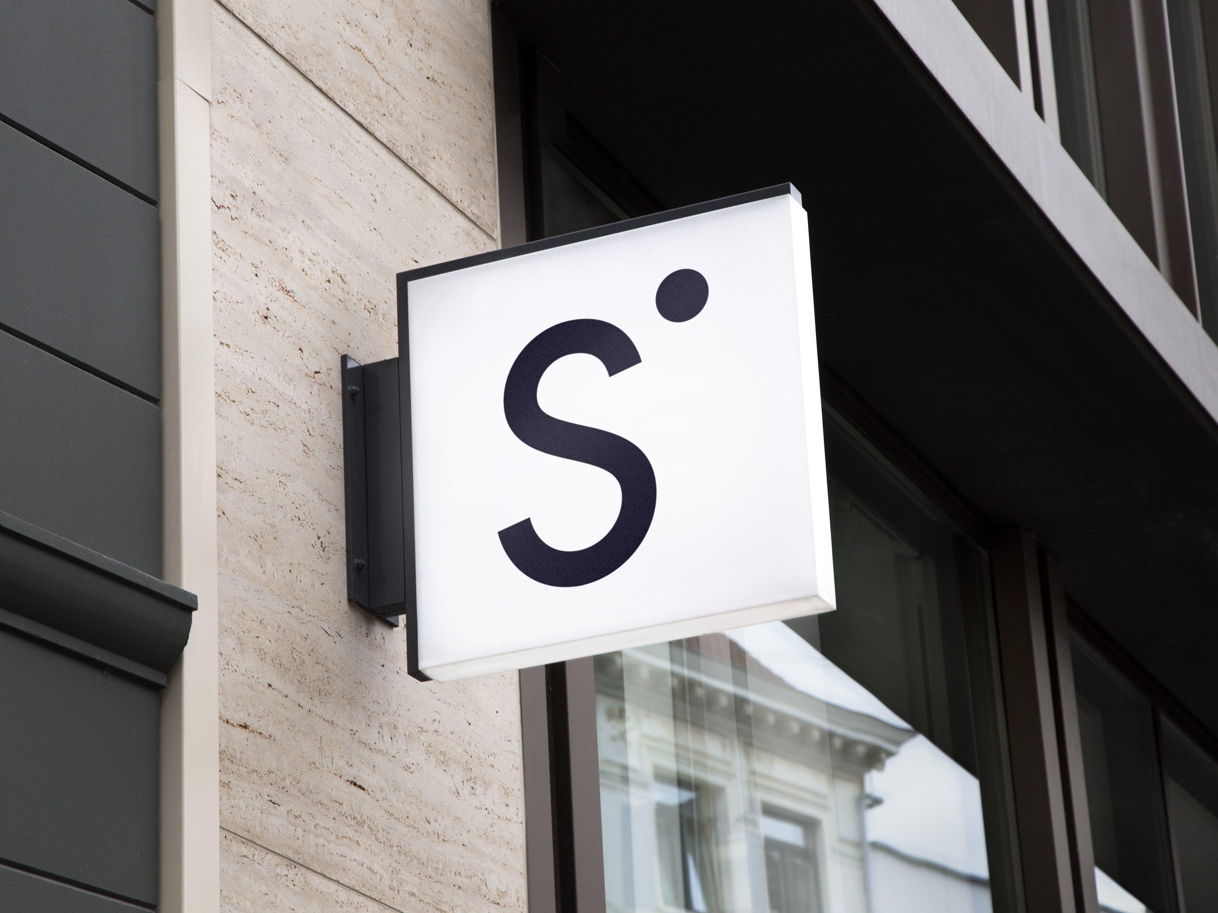 Bildet viser et skilt på en bygning med Sbankens logo – en sort S med en rund apostrof i øvre høyre hjørne