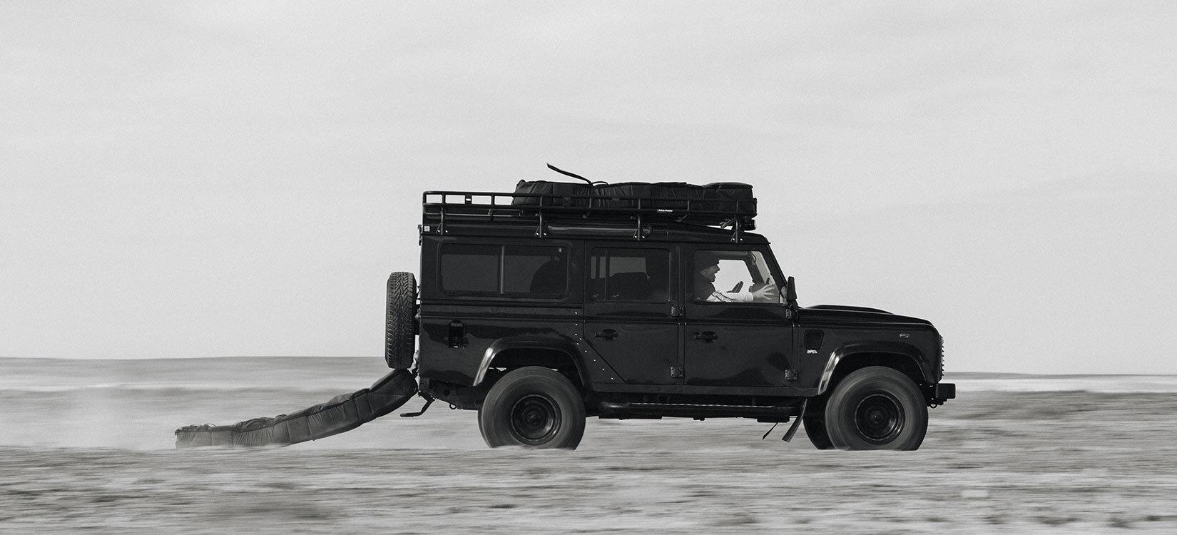 Foto av en bil i fart – tilsynelatende på en sandstrand – med en bag hengende etter.