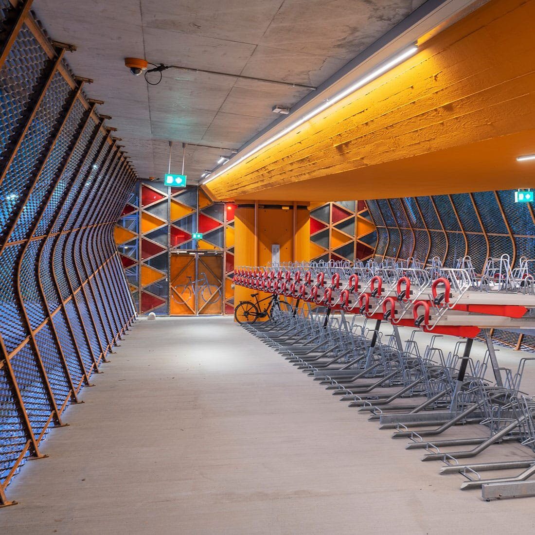Bildet viser interiøret i sykkelhotellet. Gulmalt tak og to-etasjes sykkelstativ i midten av rommet.