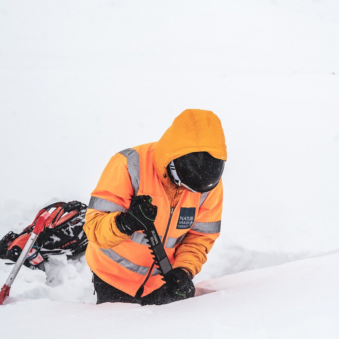 Bildet viser en person som står i dyp snø med en snøsag i hendene.