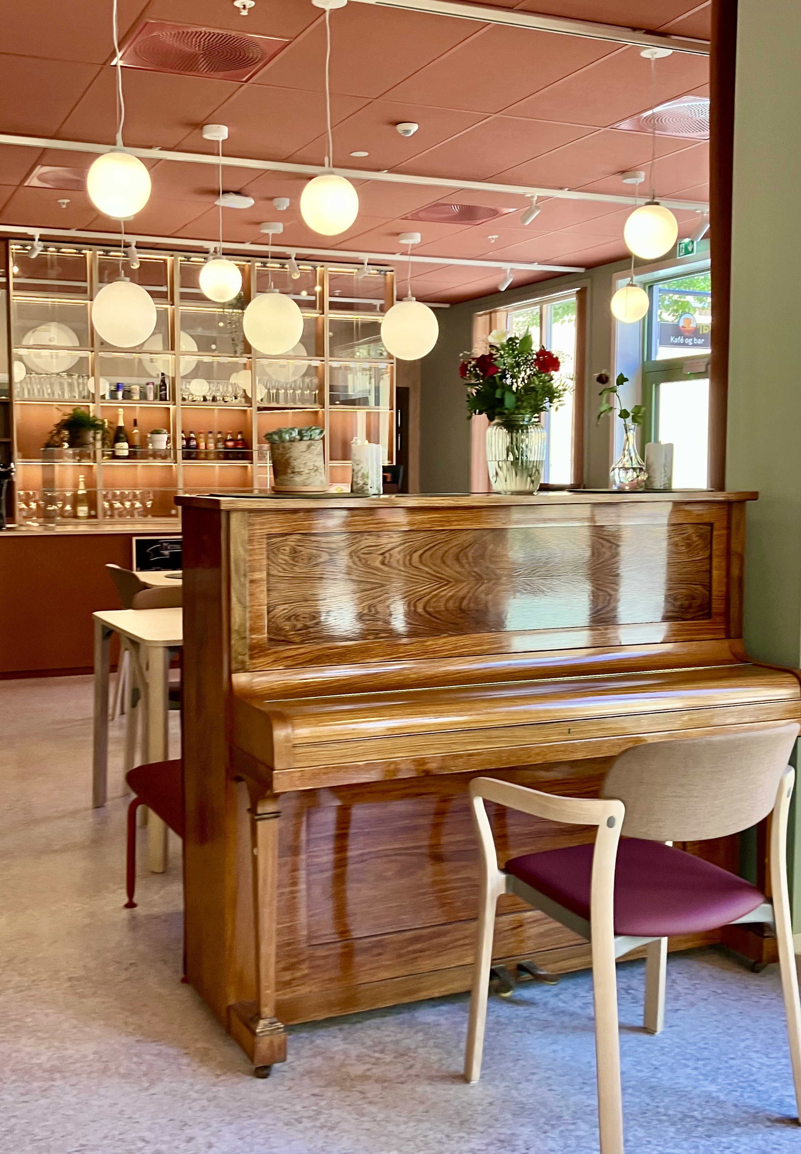 Et hyggelig og lunt rom med hyller med flasker og glass, et piano og store runde lamper.