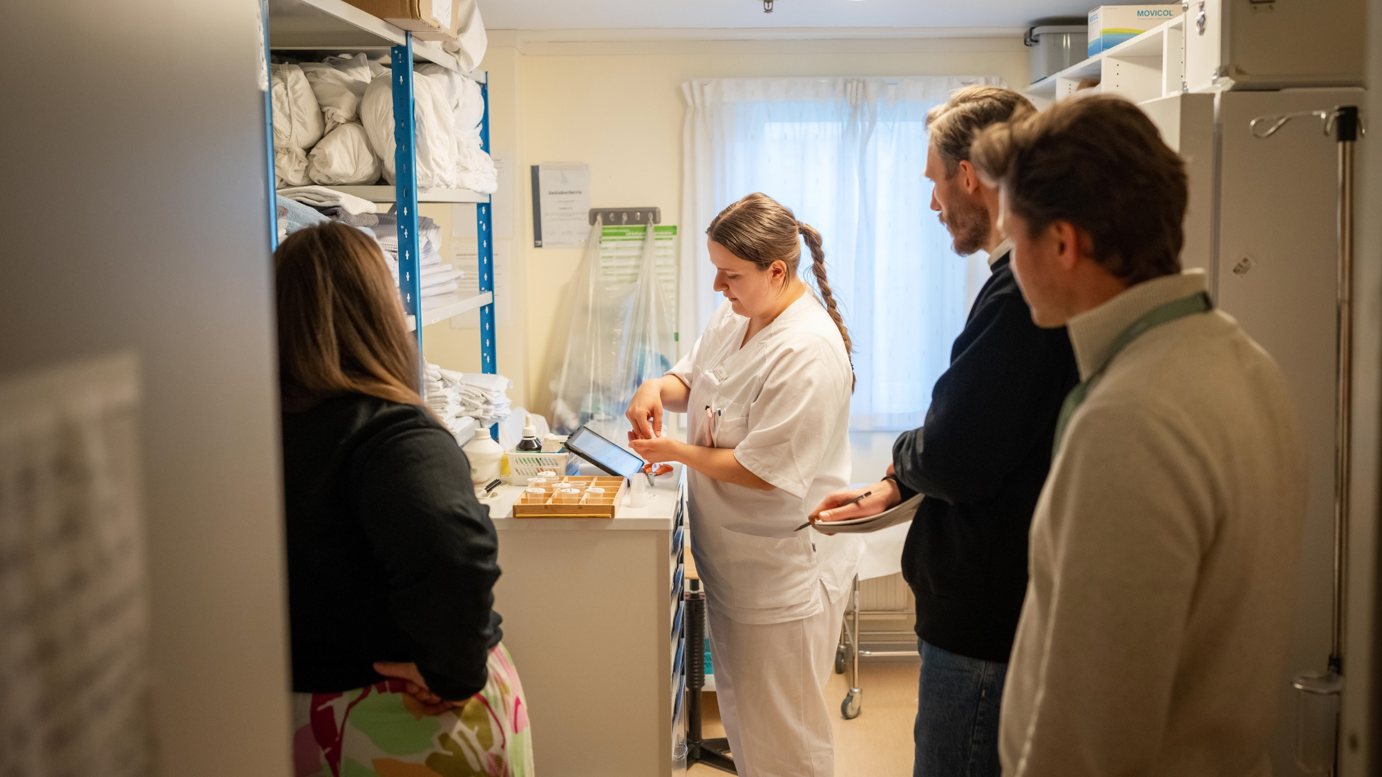 Tre personer observerer en sykepleier mens hun arbeider.