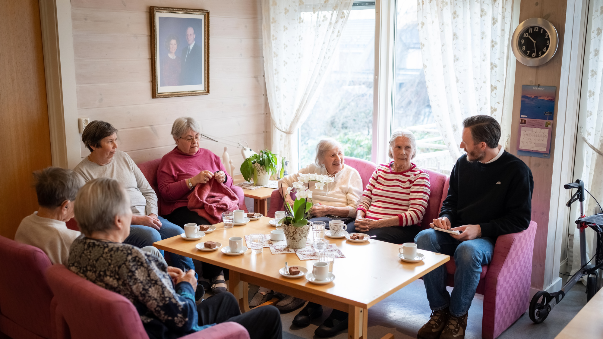 Eldre kvinner rundt et kaffebord i samtale med en yngre mann.