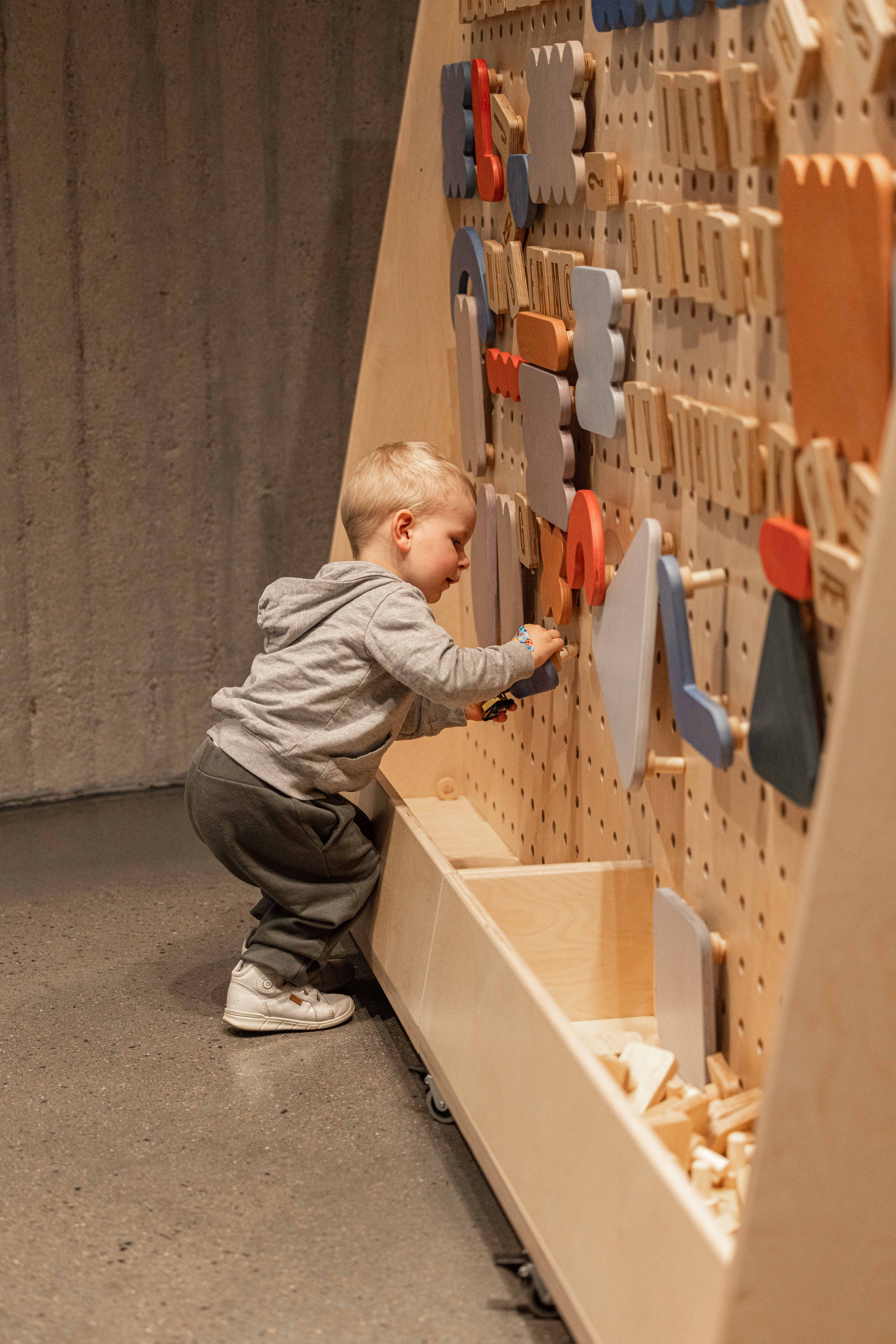 Foto av et lite barn står foran en  tavle der det kan henges opp ulike figurer i tre.