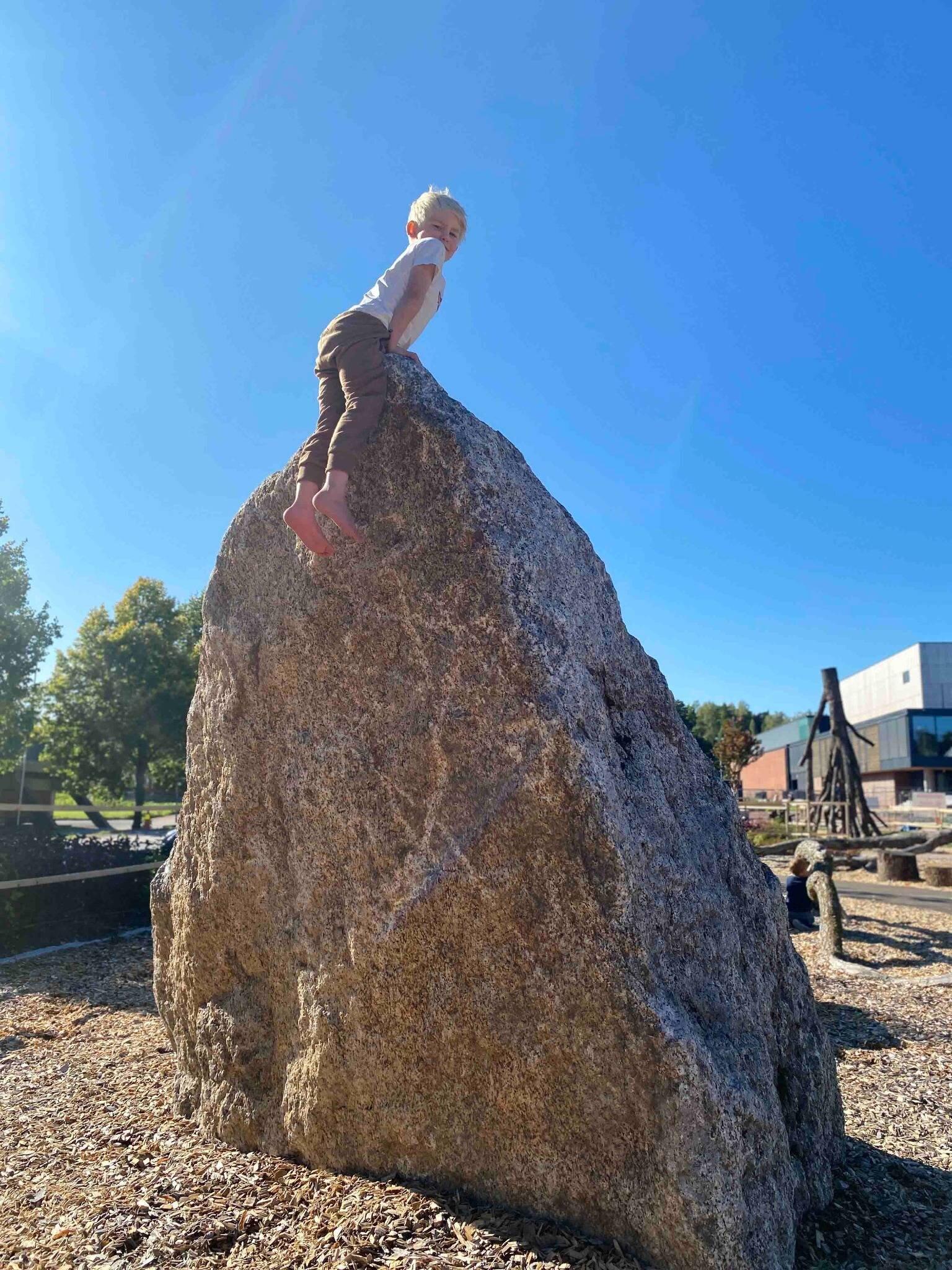 En liten gutt som har klatret opp til toppen av en enorm stein.