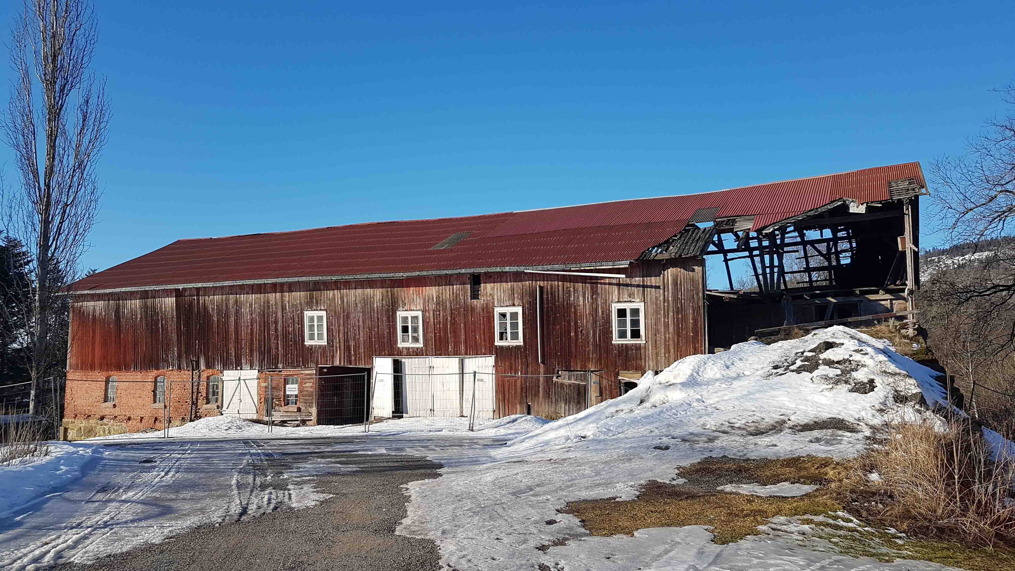 En falleferdig, brun låve med smeltende snø utenfor.