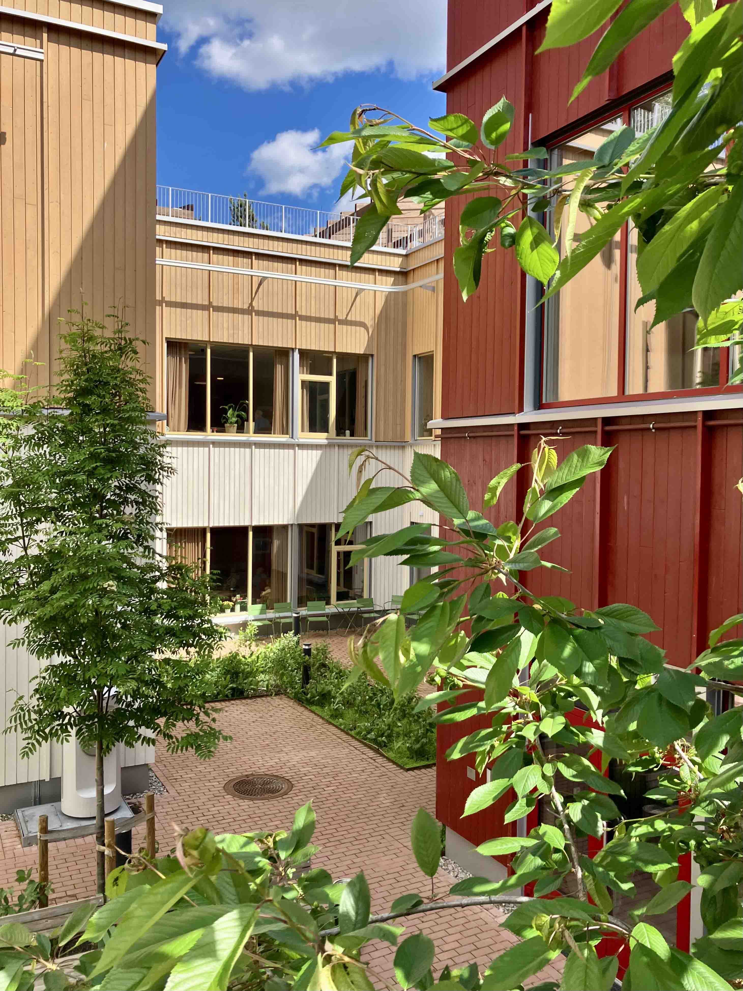 Bygninger i gult og rødt rundt en åpen plass med grønne vekster