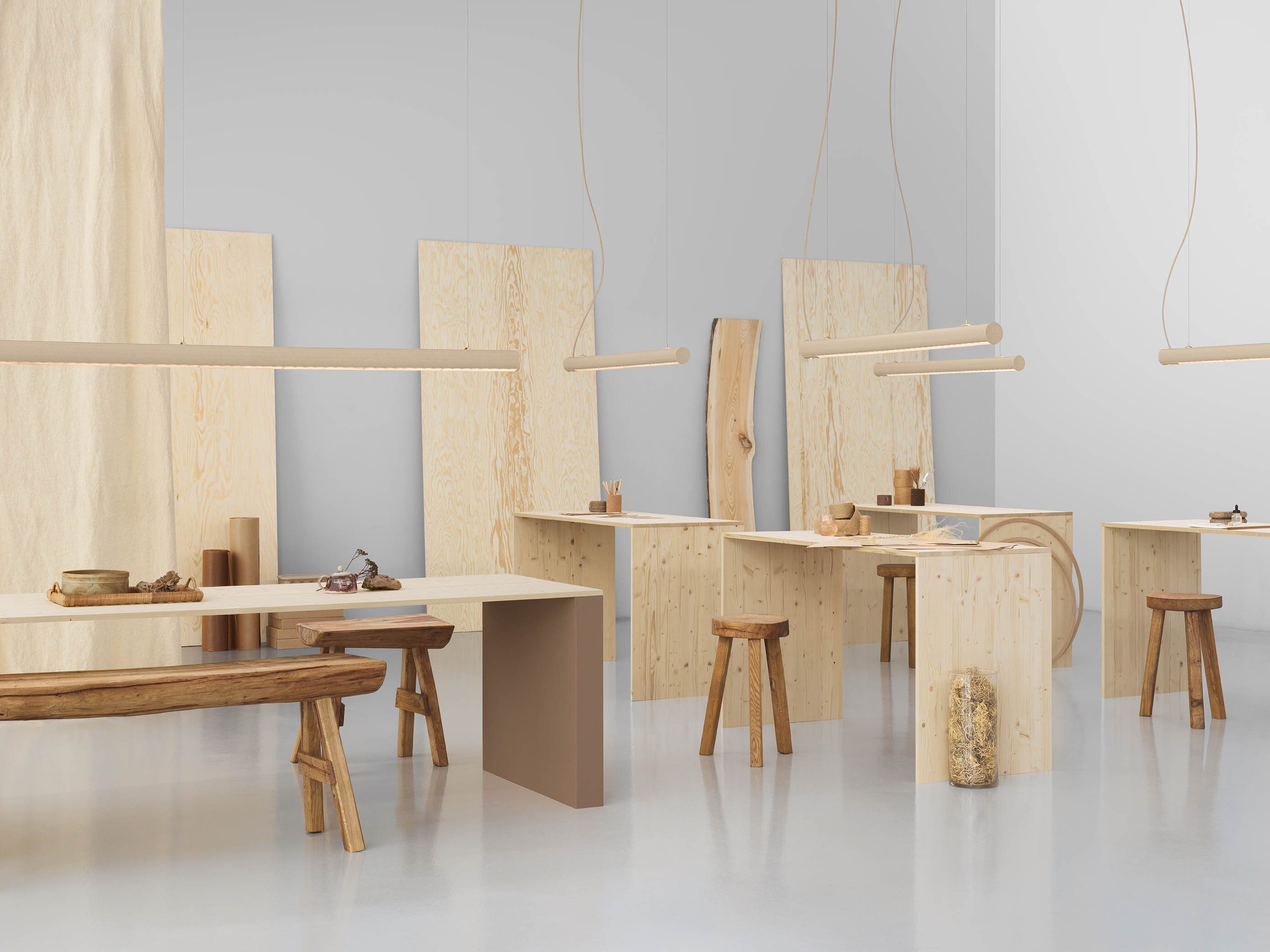 Flere benker og krakker i ulike typer treverk i et stort rom. Over benkene henger lamper av typen Superdupertube.