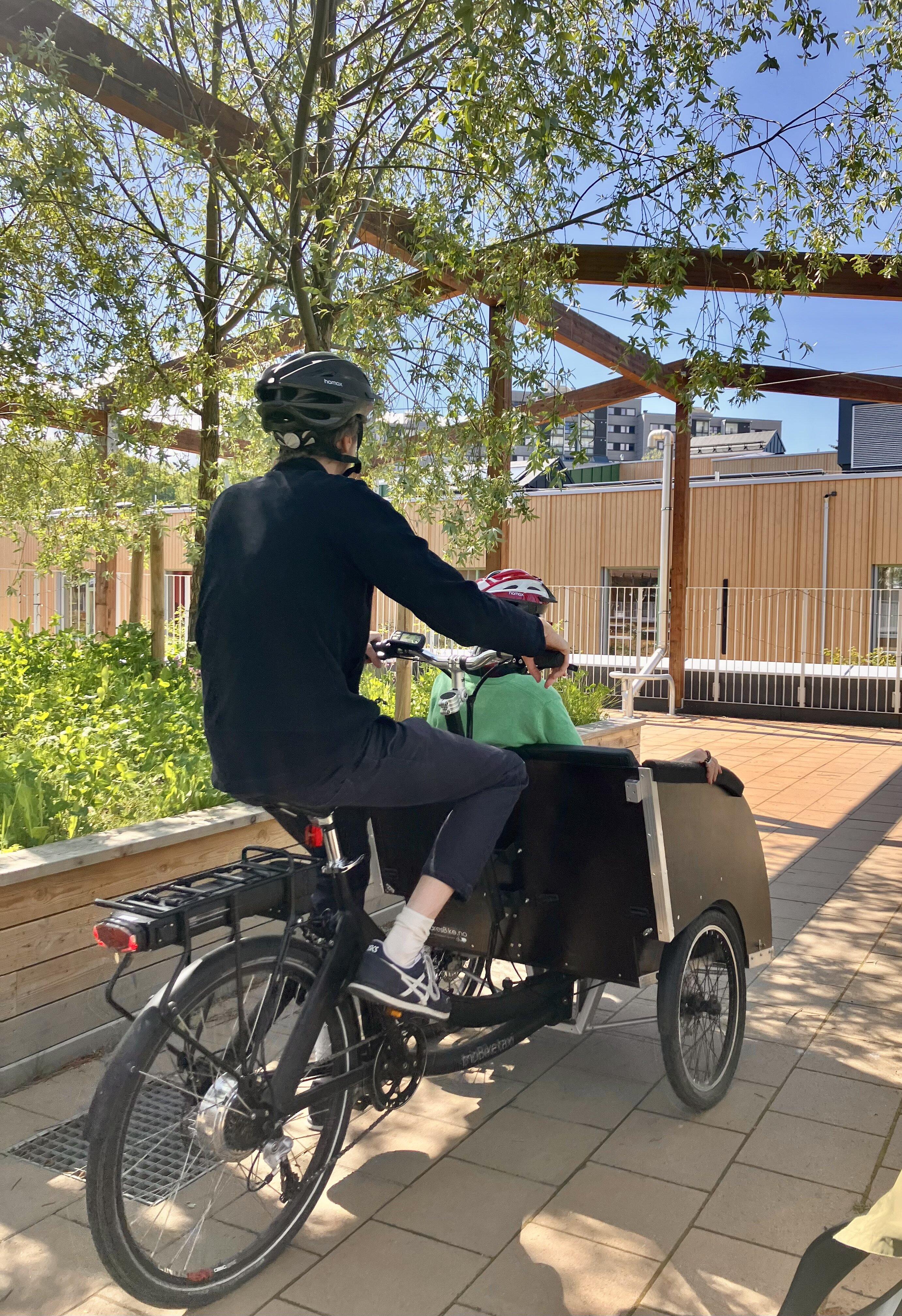 Et par på en lastesykkel, han sykler, hun sitter i kassen foran.