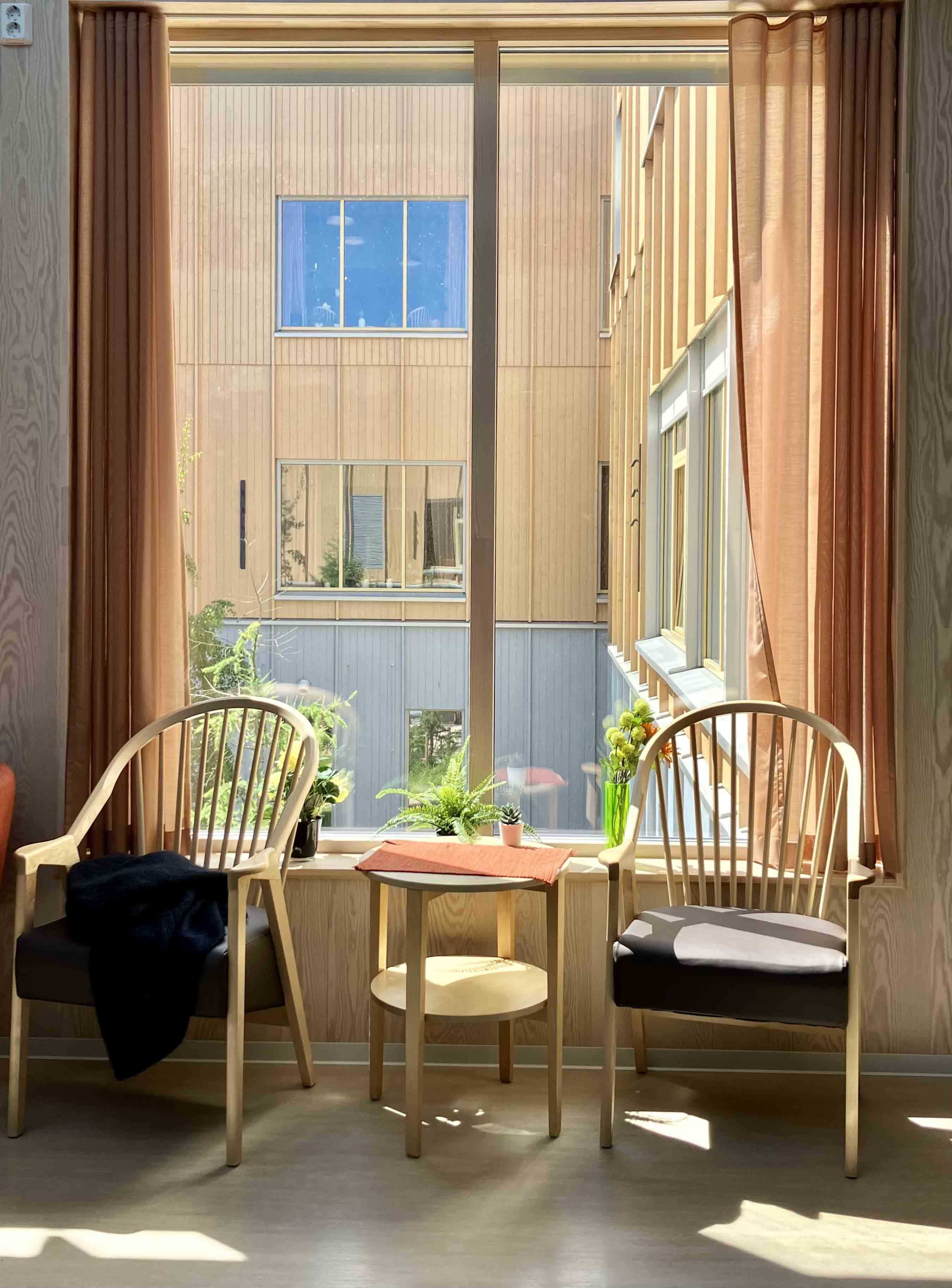 To pinnestoler og et lite bord foran et vindu med utsikt mot en bygning med hyggelige vinduer.