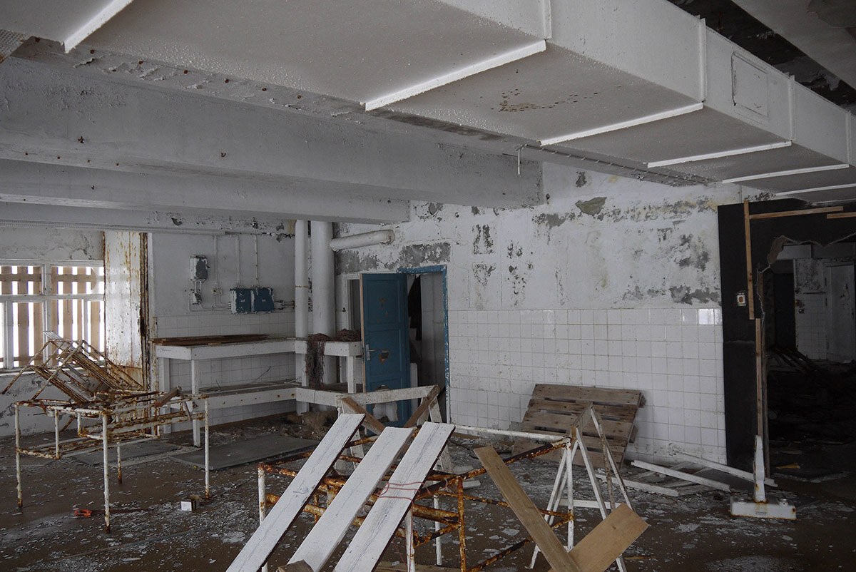 Et nedslitt, forlatt fabrikklokale, med avflasset maling og rustne hyller og løse materialer.