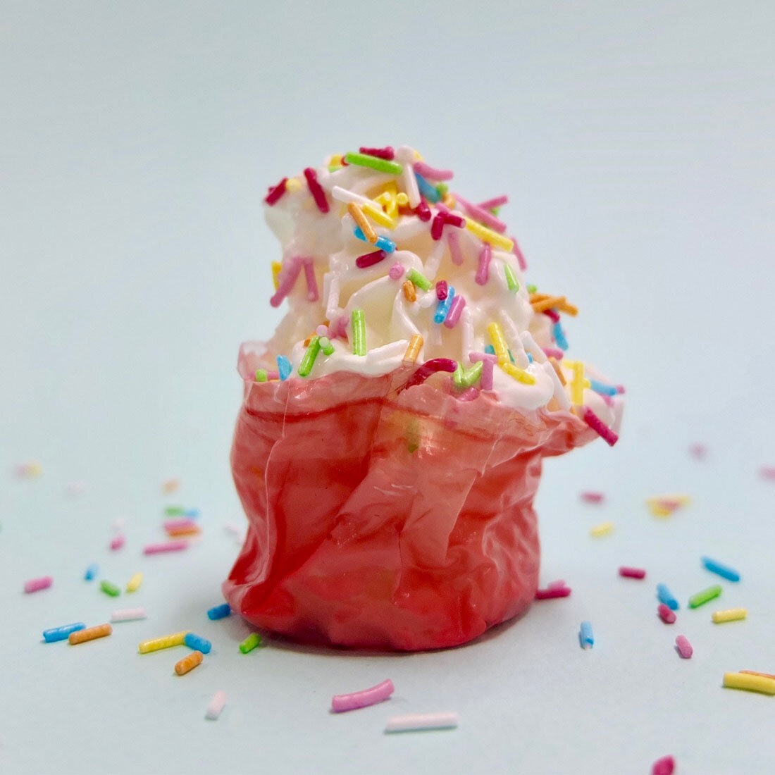 Krem med flerfarget strøssel i en rød form som minner om en muffinsform, men er laget av alginat.
