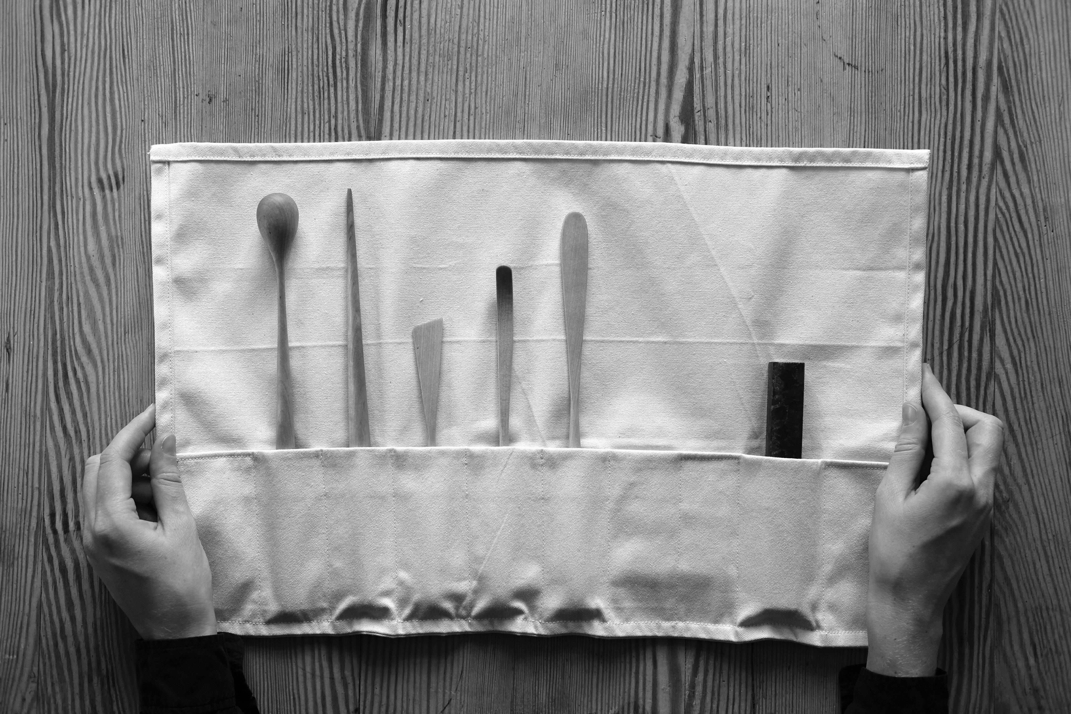 Et sort/hvitt foto av bestikkdeler ryddig plassert i en sammenrullbar lerretsmappe.