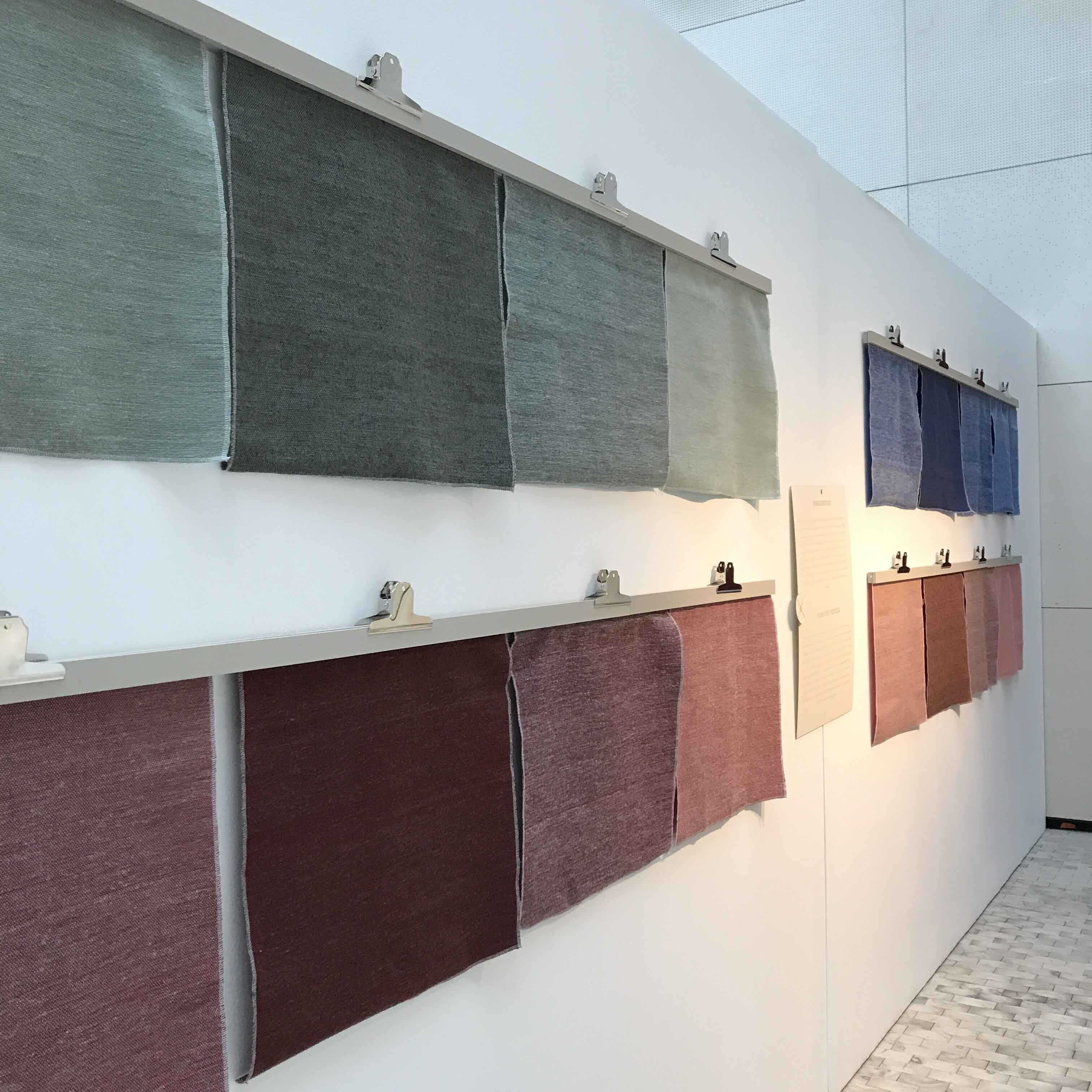 Stoffprøver i ull, i mange ulike farger, hengende på rekke og rad på veggen.