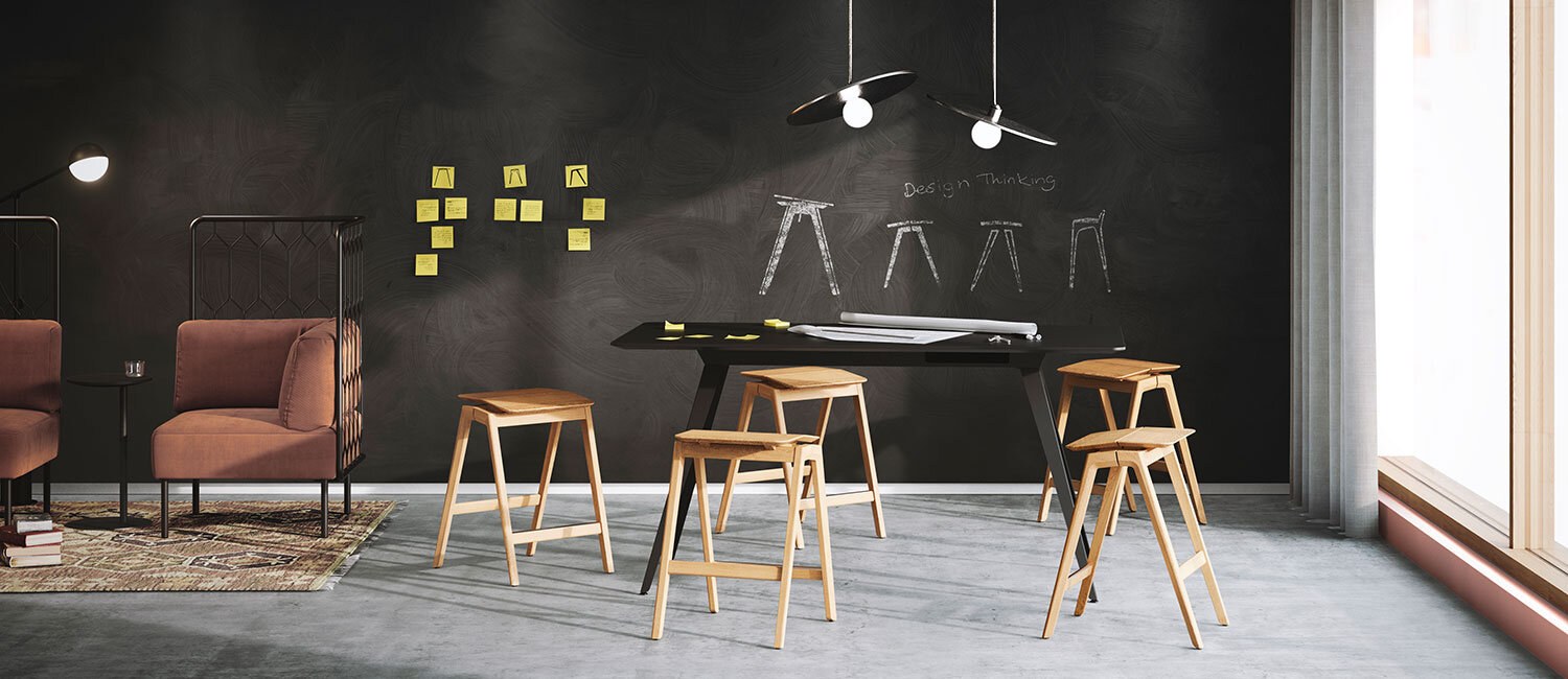 Fem trekrakker med vinklede sitteplaser står plassert rundt et sort bord i en kontorsetting med postits og skisser på bakveggen.