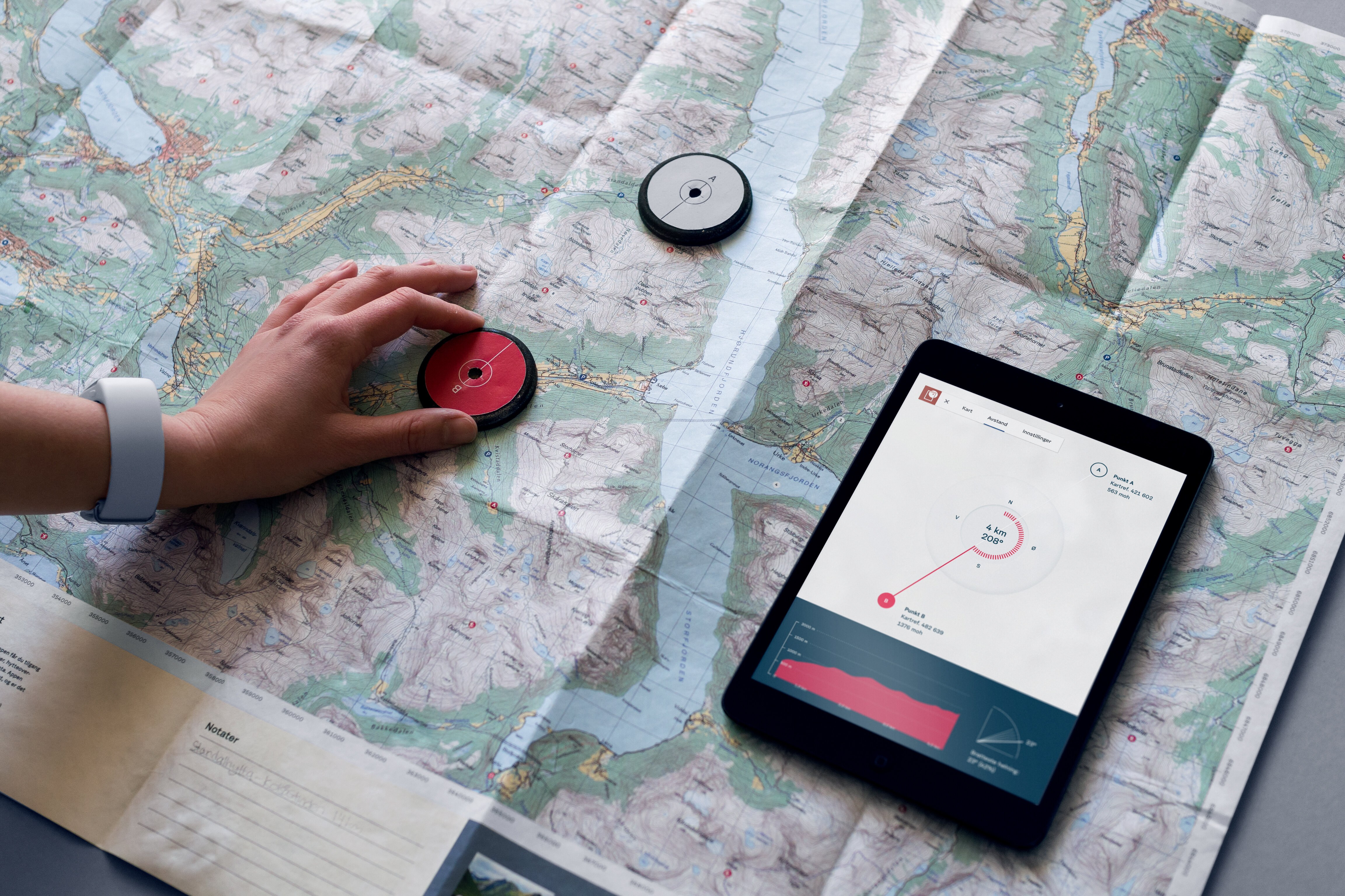 Bildet viser to runde sensorer som er plassert oppå et utbrettet kart. Ved siden av ligger en ipad, som viser detaljer om strekningen mellom de to sensorene.