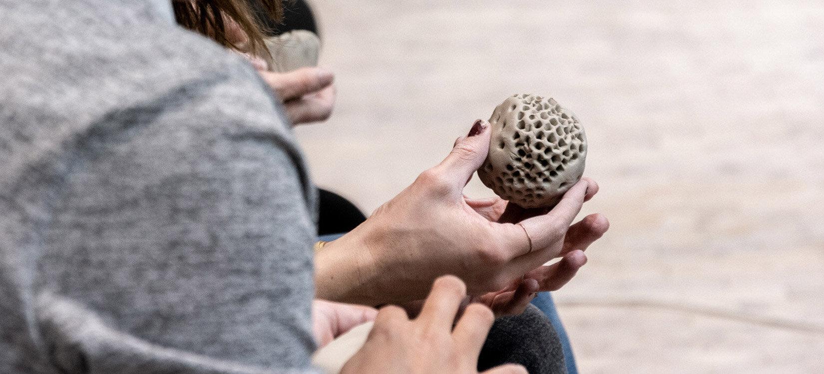 Nærbilde av hendene til en person som holder en rund hullete leireball