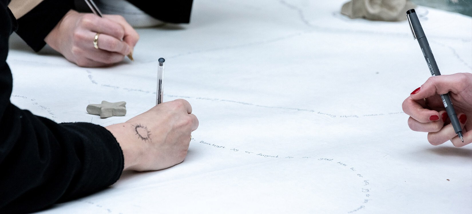 Nærbilde av tre hender som tegner eller skriver på et stort hvitt ark.