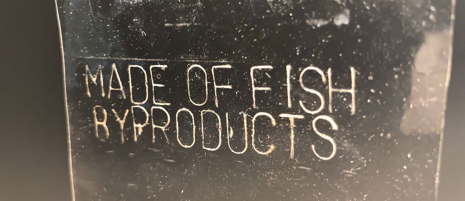 Et nærbilde av tekst risset inn i et gjennomsiktig materiale: "Made of fish byproducts"
