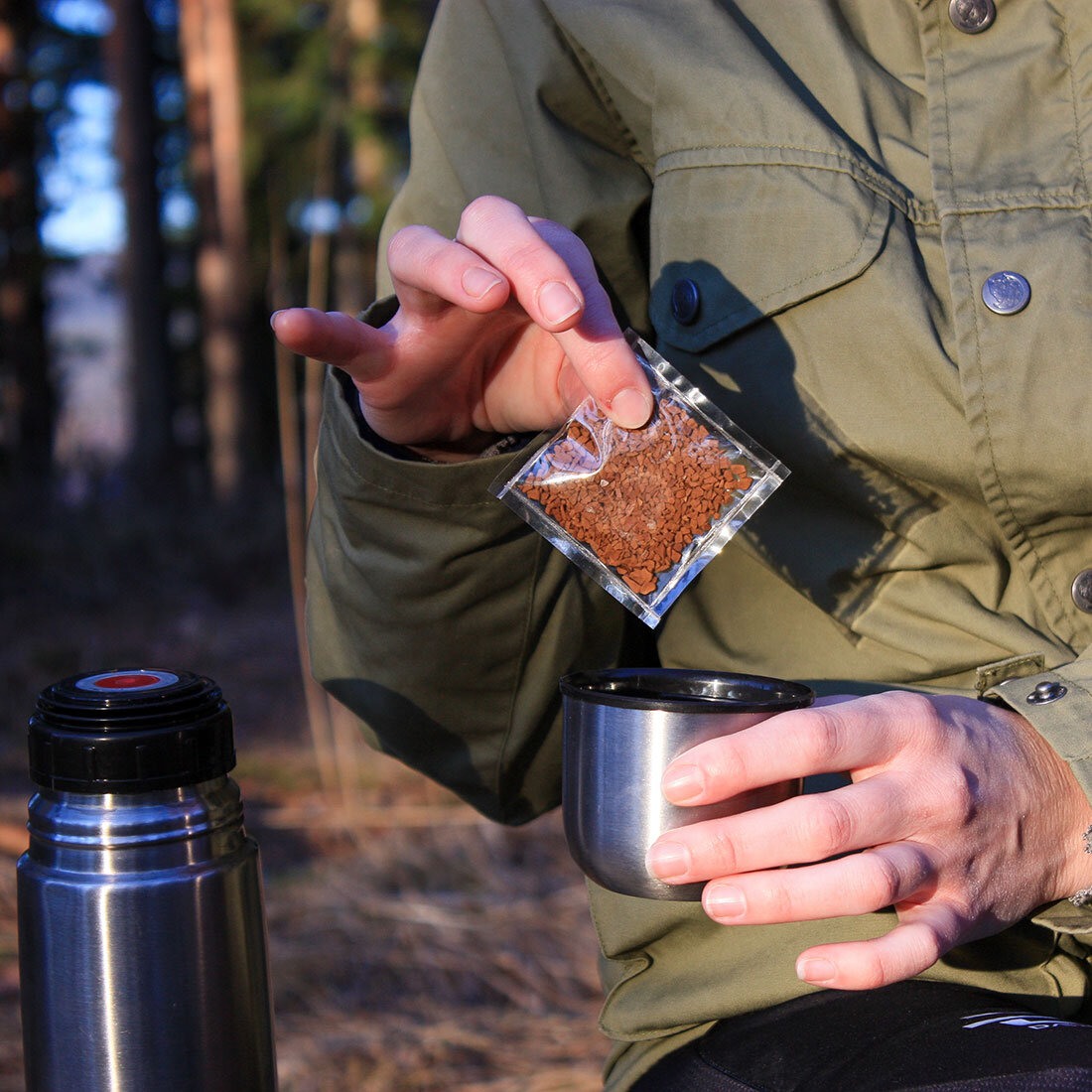 Bilde som illustrerer bruksområde for SLOG: En person i en skog er i ferd med å hive en emballert porsjonspakning med pulverkaffe i en termos.