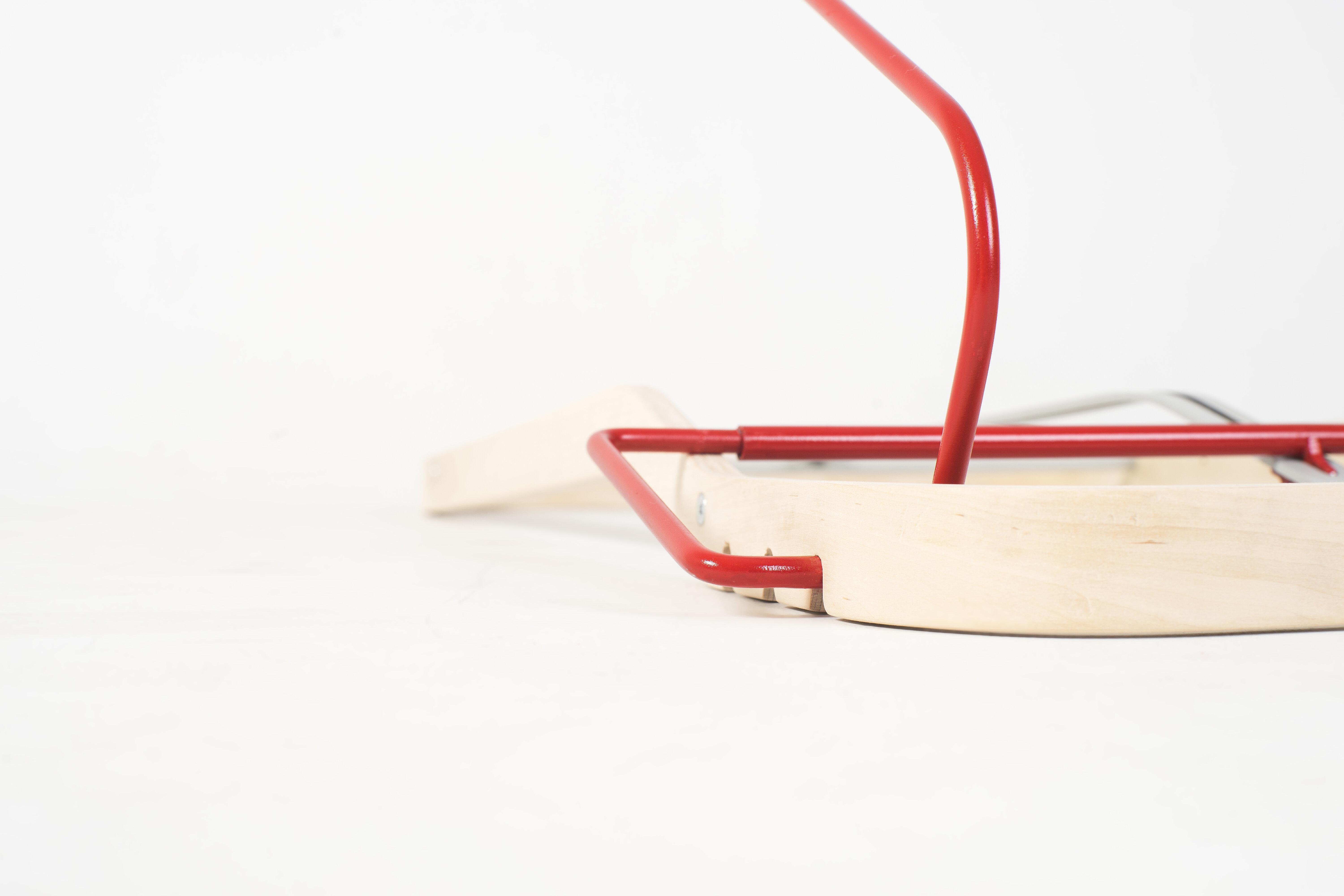 Et detaljfoto av basen på stolen hvor den røde metallrammen er festet i trestativet som utgjør basen på stolen.